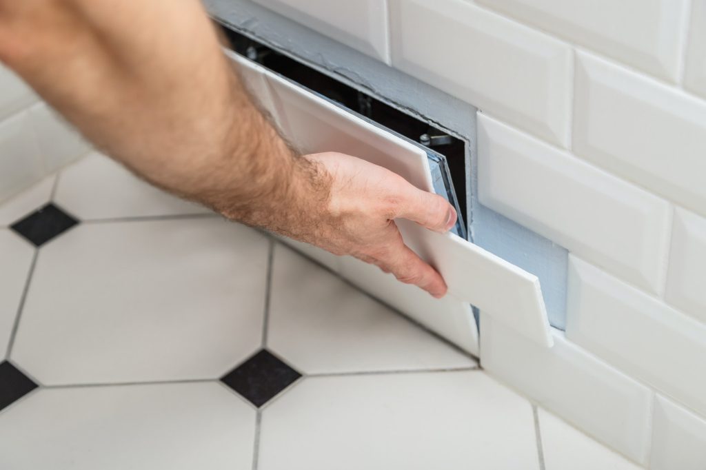 Open hidden revision sanitary hatch on the wall of tile under the bathroom